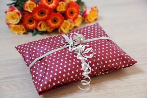 Parcel wrapped in heart patterned paper and beautiful flowers on wooden tab.. Foto stock