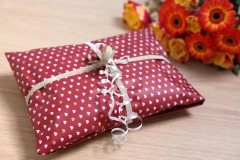 Parcel wrapped in heart patterned paper and beautiful flowers on wooden tab.. Stock Photos