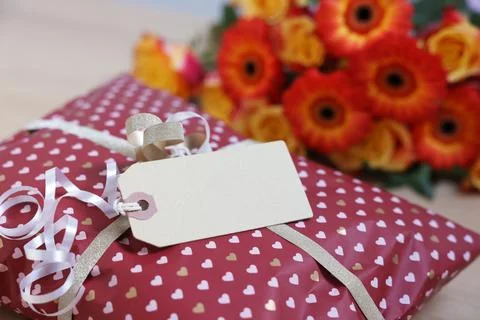 Parcel wrapped in heart patterned paper with cardboard tag and flowers on t.. Stock Photos