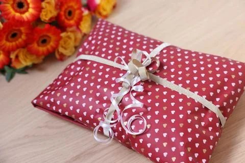 Parcel wrapped in heart patterned paper and beautiful flowers on wooden tab.. 스톡 사진