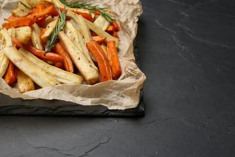 Parchment with tasty baked parsnip and bell pepper on dark grey table, clos.. Stock Photos
