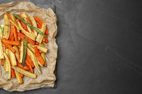 Parchment with tasty baked parsnip and bell pepper on dark grey table, top .. Stock Photos