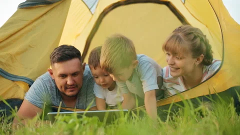 Parent and child playing internet computer laptop together in a yellow tent Stock Footage 128983539