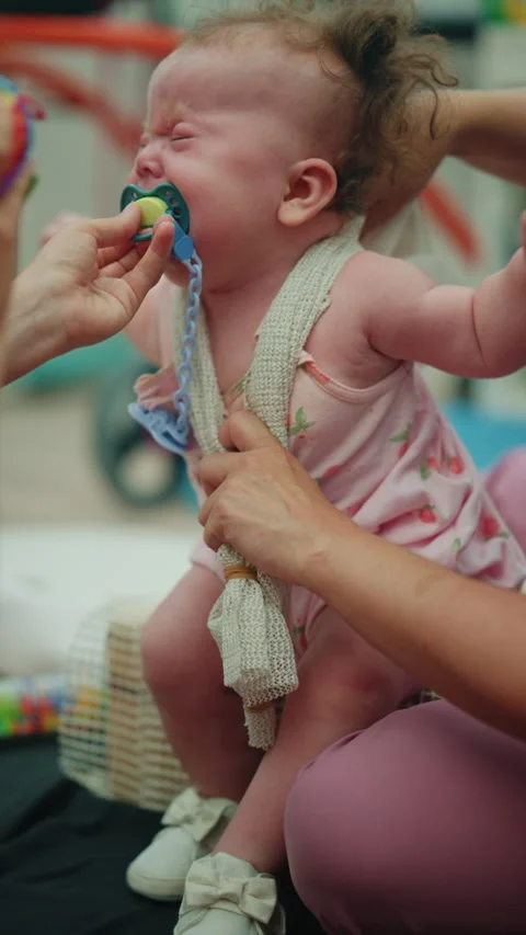 Parent carefully giving a pacifier to a crying infant, providing comfort and Stock Footage 339791867