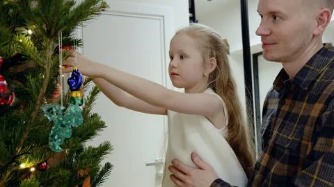 Parent carefully supporting child while hanging christmas tree ornaments Stock Photos