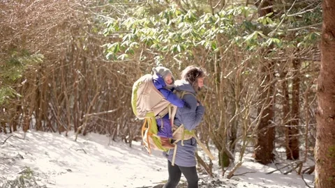 A parent carries their child in a backpack carrier while hiking through a snowy Stockbeeldmateriaal 280077348