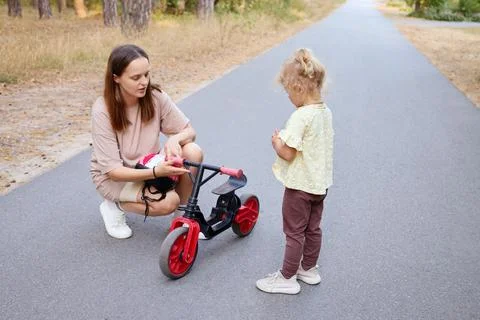 Parent guiding her toddler during bicycle training in the park ensuring safet Stock Photos