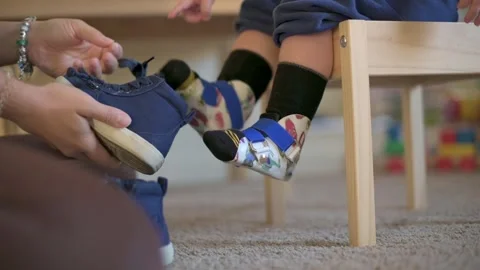 Parent holding shoe while toddler wearing orthopedic braces with blue straps Stock-Footage 295839106
