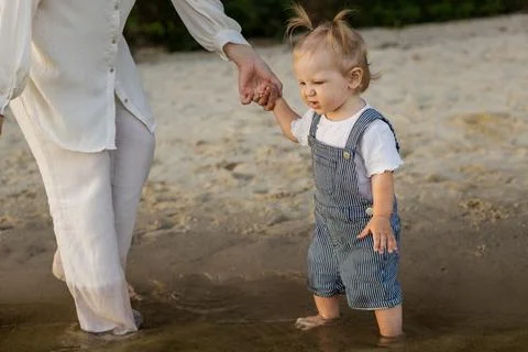 Parent holding toddler's hand while walking on wet sand at the beach Stock Photos