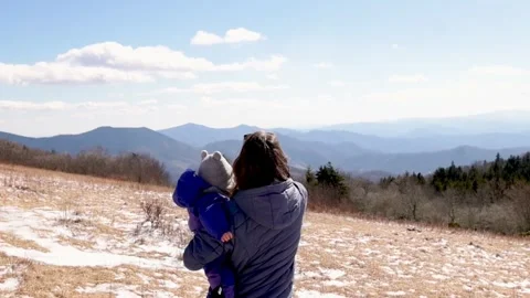 A parent holds their child while admiring a scenic mountain view on a sunny Stock Footage 280020130