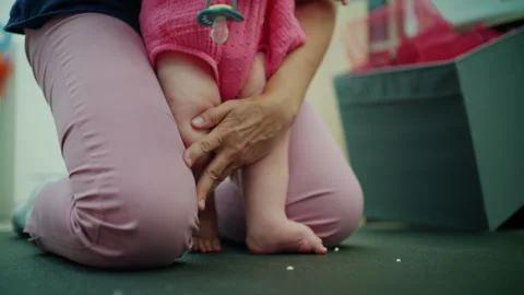 Parent kneeling, supporting baby taking first steps on a floor, fostering Видео 342755245