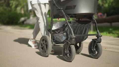 Parent pushes stroller. Stroller navigates sunlit pathway. Urban parent tests Video stock 346402965