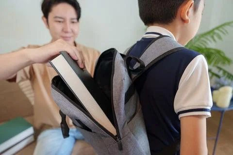 Parent putting textbook into child backpack for back to school preparation Stock Photos