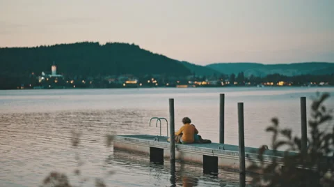 A parent reading a book to her child on the end of a quay during sunset Video stock 63224610