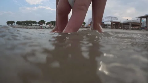 Parent standing in shallow ocean water, helping a baby taking first steps on a Видео 343331222