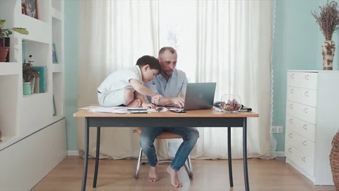 Parent working online from home at the table. A little boy sitting on the table Stock Footage 129368413