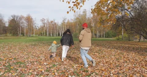 Parents and child running through leaves together in scenic autumn park Stock Footage 336531039