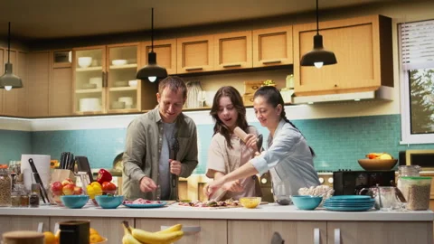 Parents and daughter doing karaoke and dancing together while cooking Stock Footage 326368564