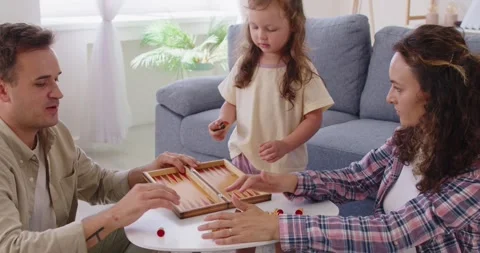 Parents and daughter playing backgammon together on a coffee table in a cozy Stock Footage 330134973