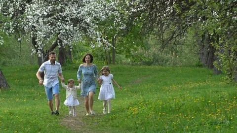Parents and daughters run in spring park in blooming tree garden. Slow motion Stock Footage 119356018