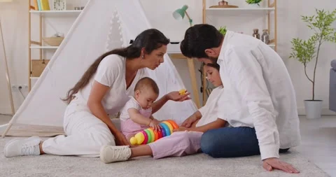 Parents and kids sharing stacking ring toy on floor in cozy home interior Stock Footage 318429080