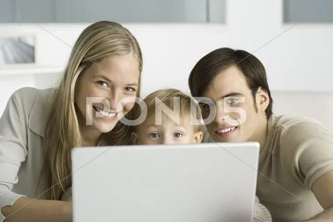 Parents And Young Son Using Laptop Computer, Smiling At Camera