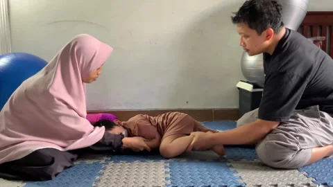 Parents Assisting Child Physiotherapy Using Therapy Ball at Home Stock Footage 326844661