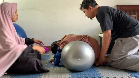Parents Assisting Child Physiotherapy Using Therapy Ball at Home Stock Footage 326844784