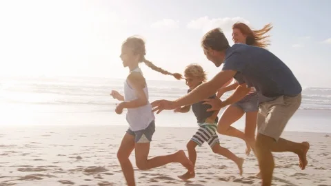 Parents Chasing Children Along Beach On Summer Vacation Stock Footage