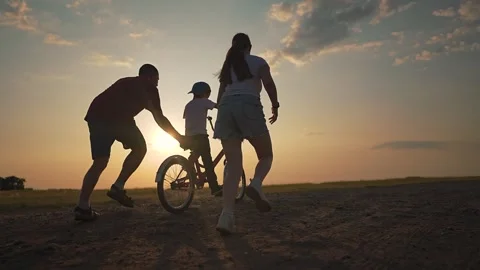 Parents guide young boy riding bike on country road during golden hour. Father Stock-Footage 311802432