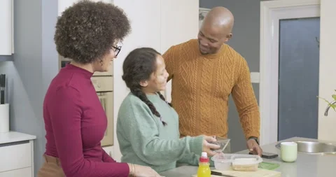 Parents guiding daughter and adding sliced bread and berries into box for school Stock Footage 335866523