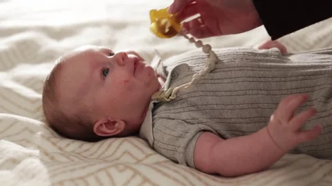 Parent's hand gently placing a pacifier into a newborn baby's mouth on a soft Stock Footage 340629908