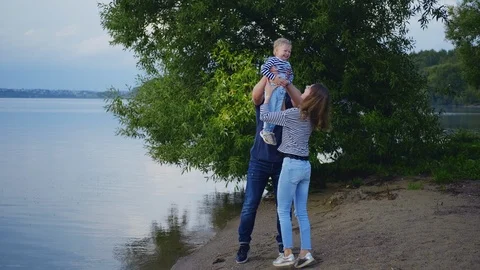 Parents having fun with their son outdoors in a park near the lake, laughing Stock Footage 115066173