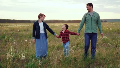 Parents hold hands of son in field of plants on cloudy day making moments Stock Footage 258963708
