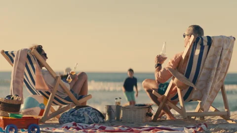Parents holding bottles of beer while their children are playing at the beach Stock Footage 262400431
