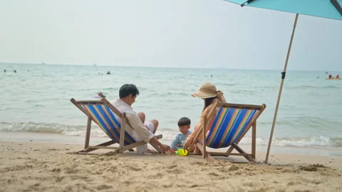 Parents sitting on beach chairs while watching their young child Stock Footage 338347675