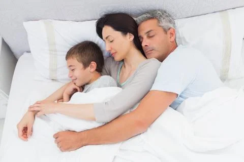 Parents sleeping with their son in bed Stock Photos