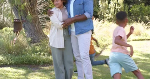 Parents standing embracing under large tree on grassy lawn with children Stock Footage 336685608
