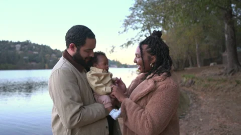 Parents standing by lakeside talking while holding their newborn baby on fall Stock-Footage 324620068