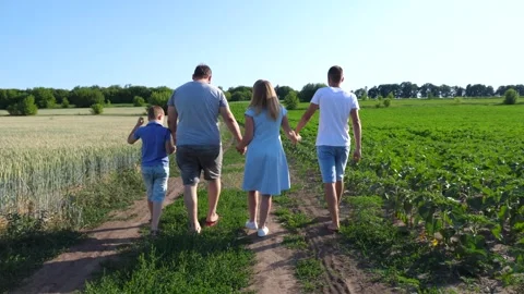 Parents with two sons hold hands of each other walking at rural road near fields Stock Footage 304111765