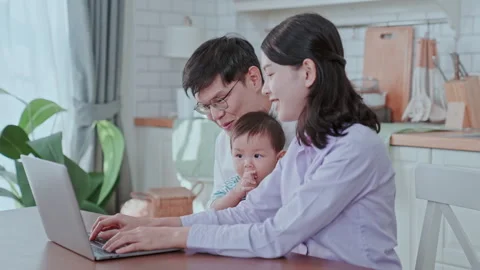 Parents working from home in a modern kitchen with their child playing nearby Stock Footage 303536078