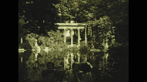 PARIS 1920s: Children sit at table on side of pond at garden. People surround Stock Footage 130357448