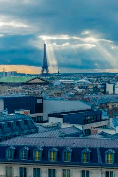 Paris skyline with rooftops and the Eiffel tower on a cloudy day with sun rays Stock Photos