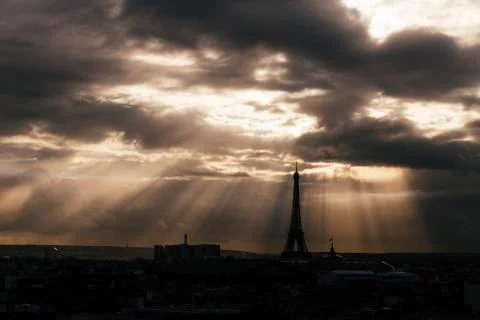 Paris skyline with rooftops and the Eiffel tower on a cloudy day with sun rays Stock Photos