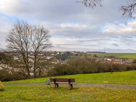 A park bench along a paved path overlooks a small village Stock Photos