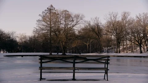 Park bench in front of frozen pond in park - Trail of cars in background Stock Footage 89944778