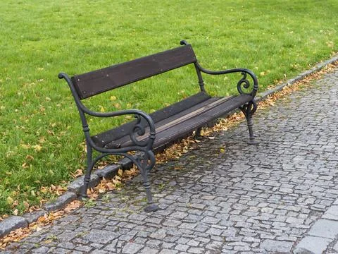 A park bench standing on the edge of a paved footpath Stock Photos