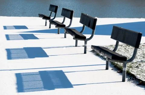 Park benches casting shadows on a light dusting of show Stock Photos