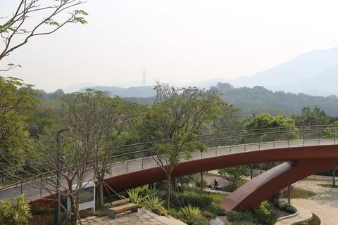 The park features an elevated walking bridge with a red steel guardrail Stock Photos