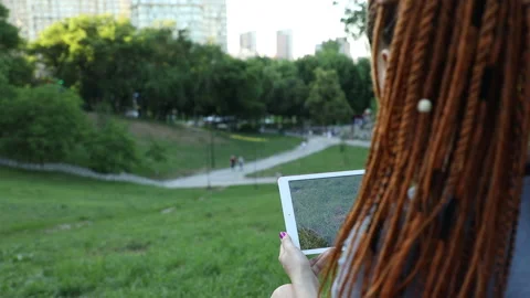 In the park, a girl with red dreadlocks makes a photo on a tablet Video stock 134913334